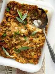 casserole dish of stuffing with fresh herbs and serving spoon.