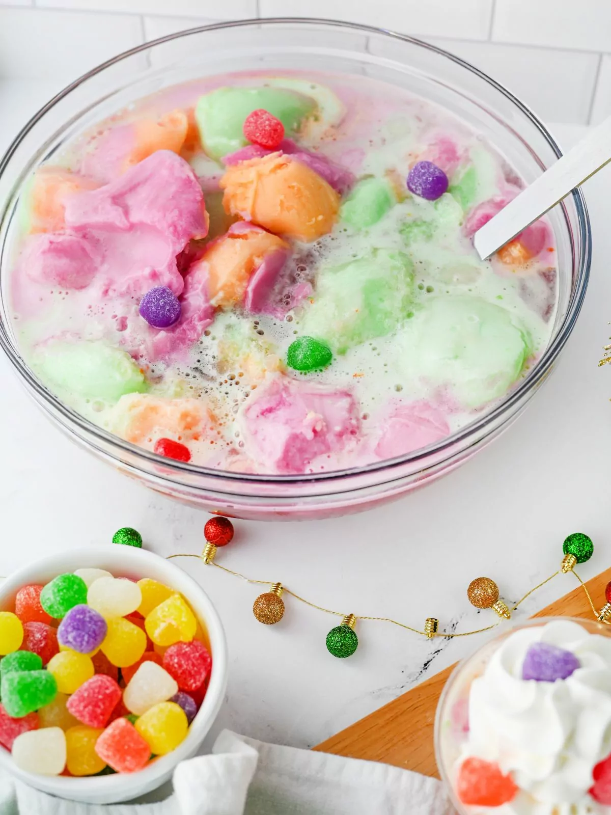 bowl of rainbow sherbet punch, a small bowl of colorful gumdrops, and a cup of punch topped with whipped topping