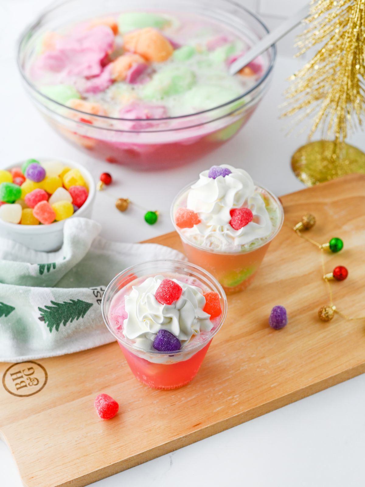 background has a bowl of colorful punch. Foreground has cups of punch with gumdrops on top