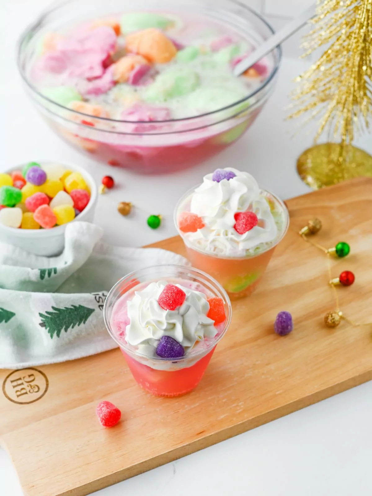 background has a bowl of colorful punch. Foreground has cups of punch with gumdrops on top