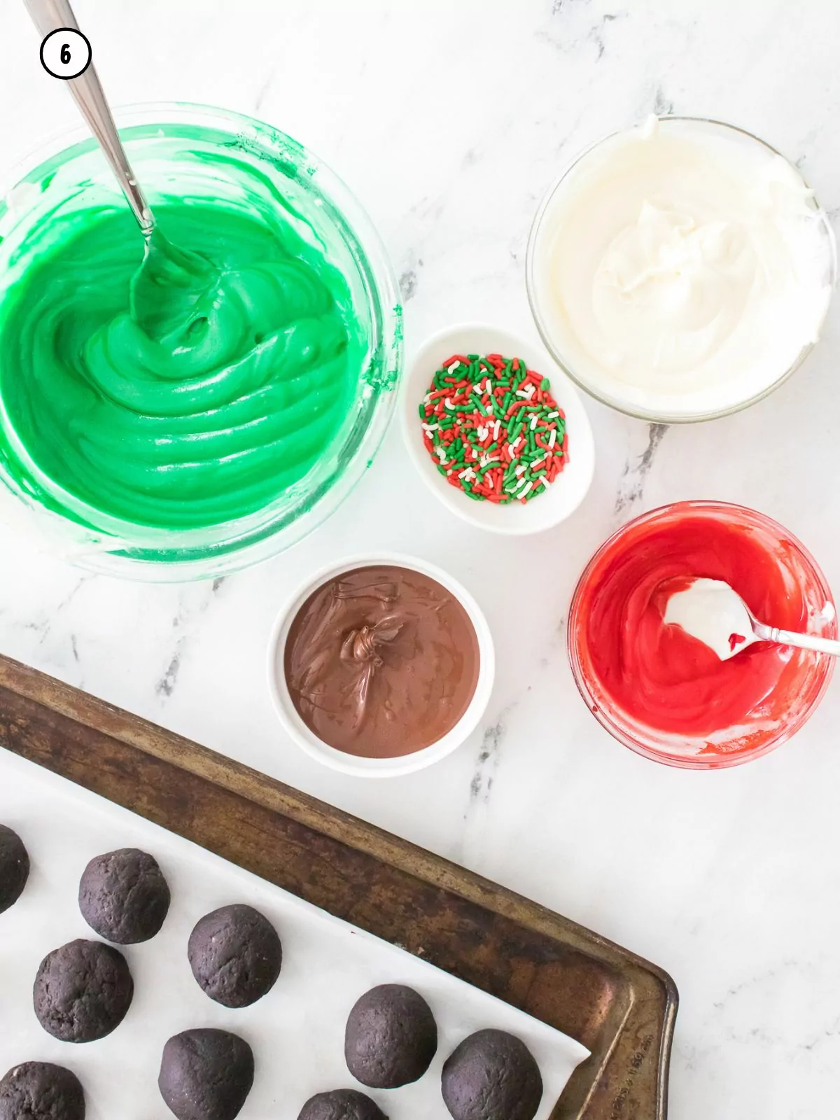 Oreo balls on baking tray with different colors of melting chocolate in small bowls.