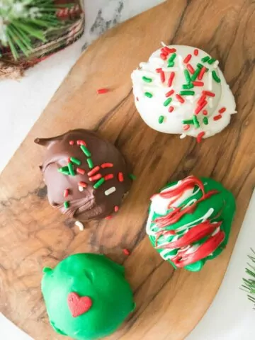 4 different colored Oreo cookie balls on cutting board decorated for Christmas.