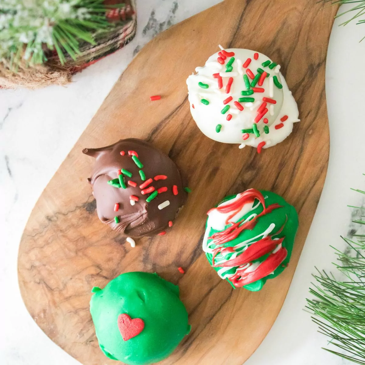 4 different colored Oreo cookie balls on cutting board decorated for Christmas.