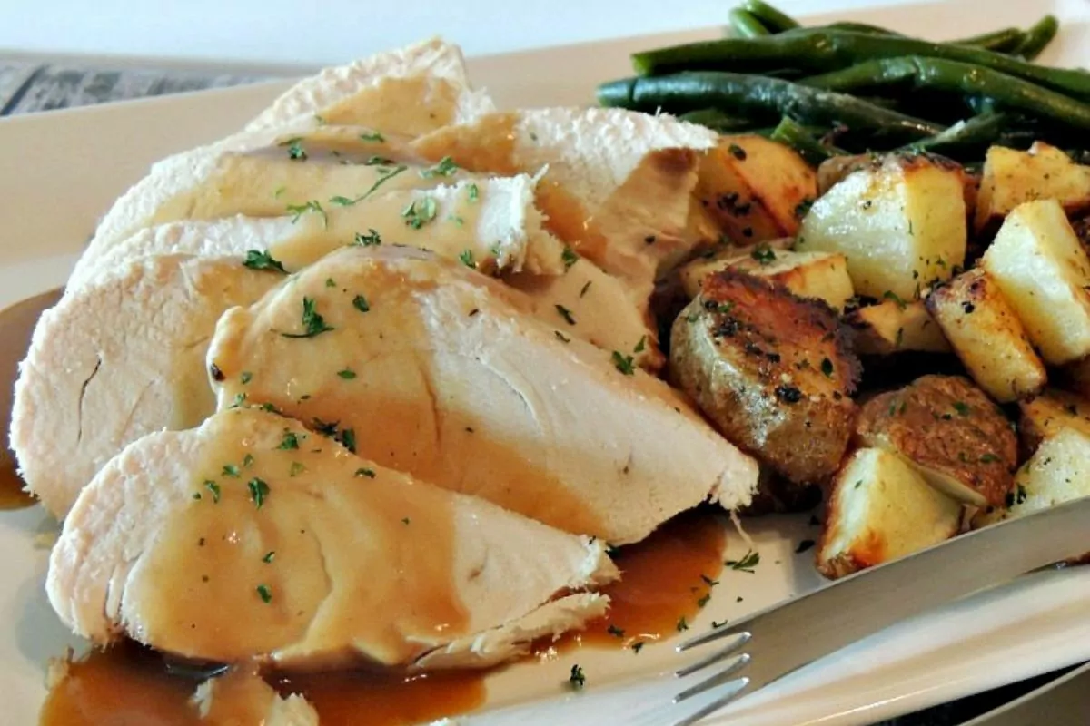 sliced turkey served on platter with gravy, potatoes and green beans.