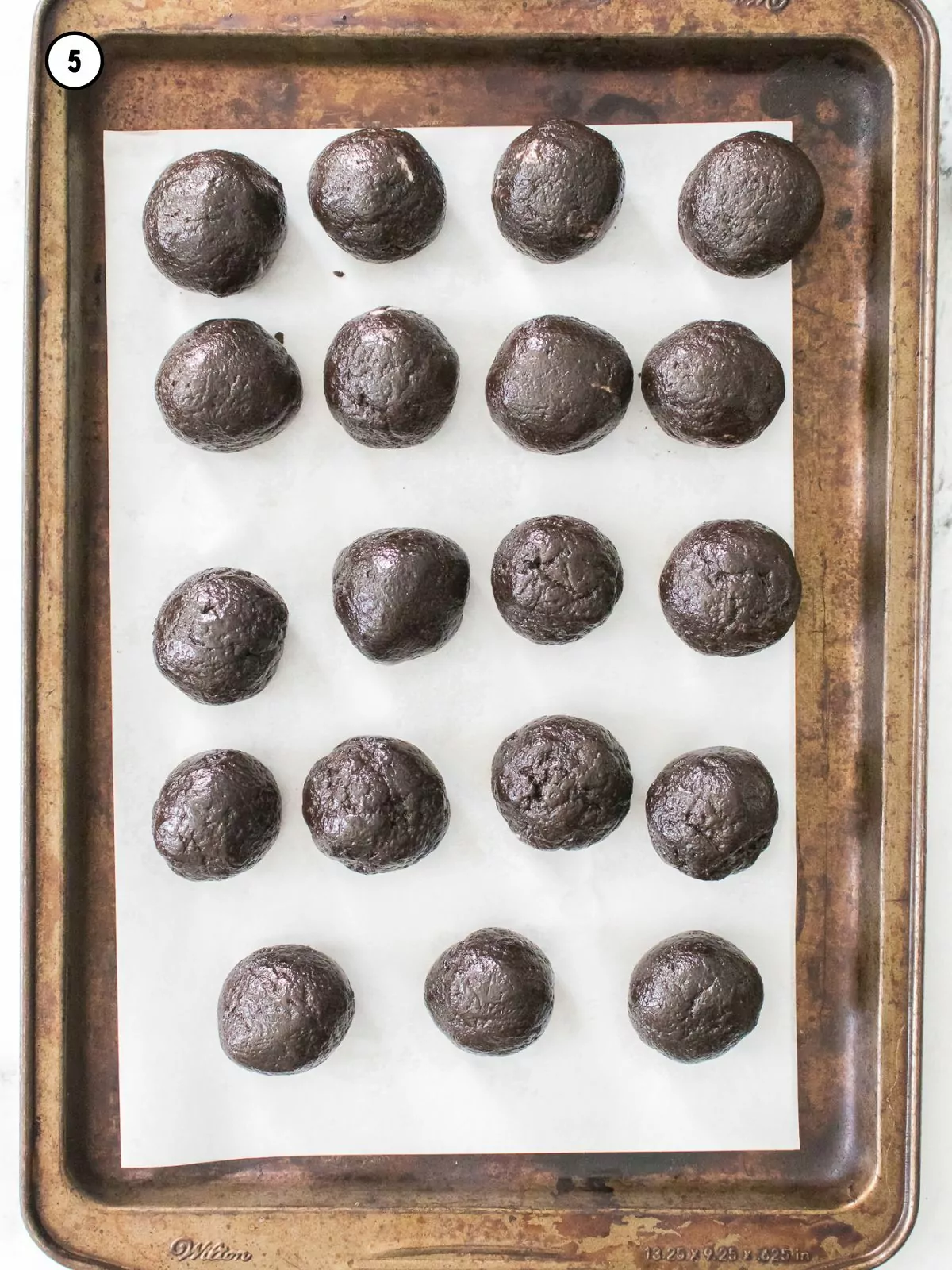 chocolate cookie balls formed and placed on baking tray with parchment paper.