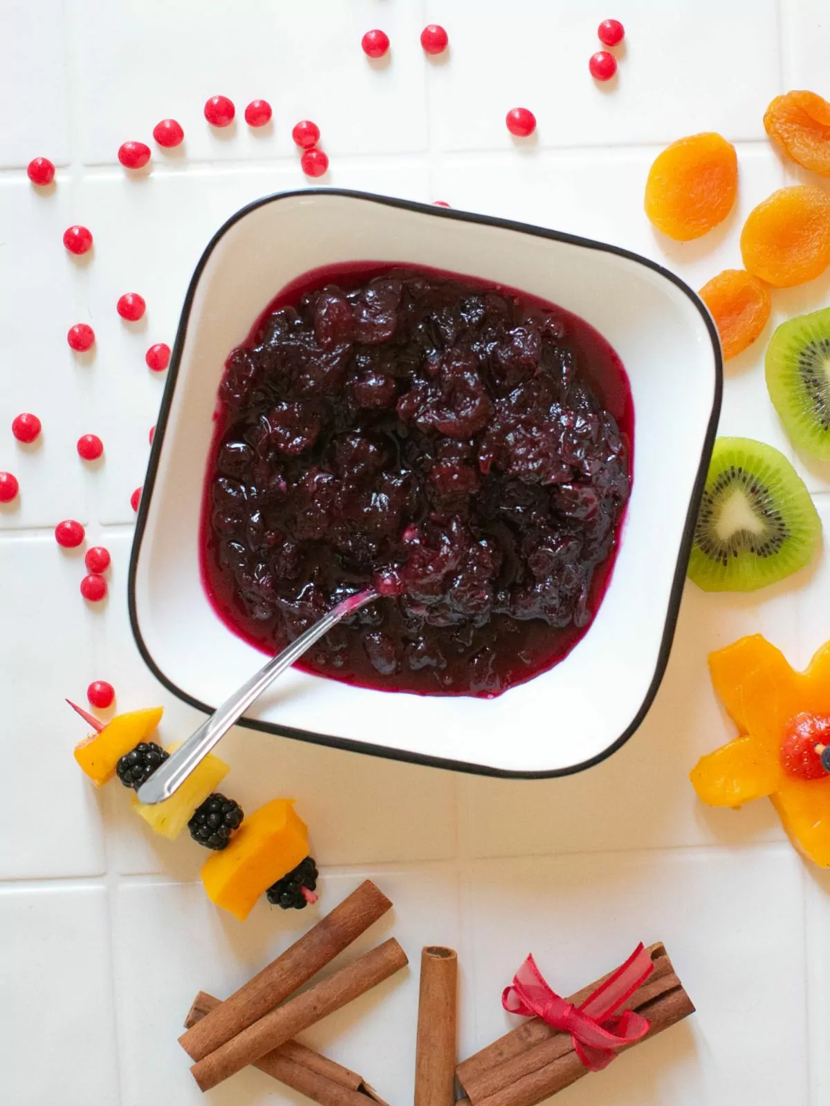 cranberry sauce in bowl with fruit and cinnamon sticks around it.