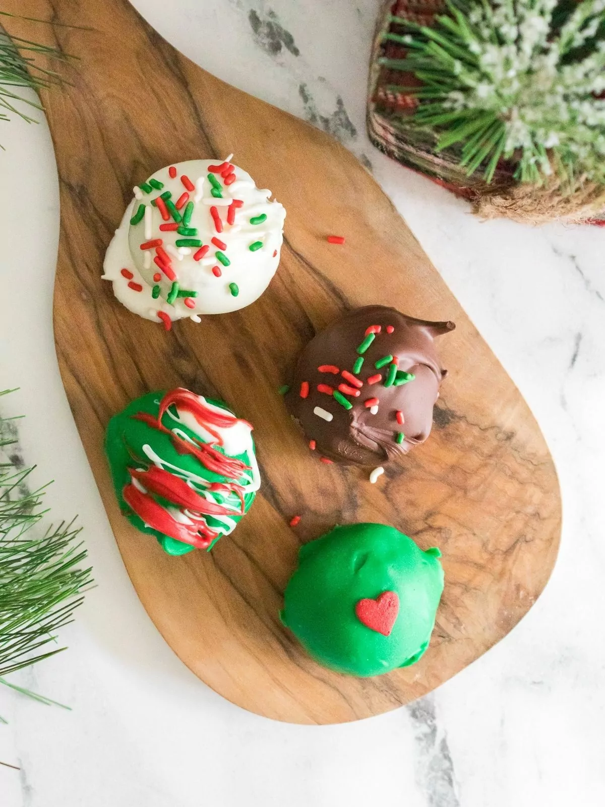 Decorated cookie balls for Christmas on a cutting board.