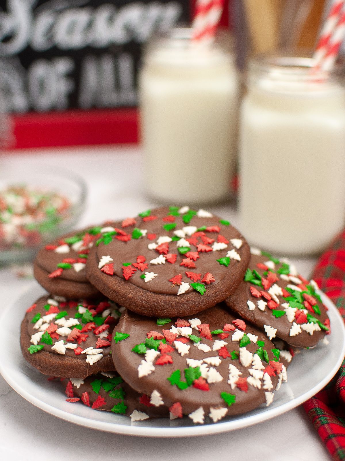 chocolate cookies with sprinkles on white plate with milk in bottles.