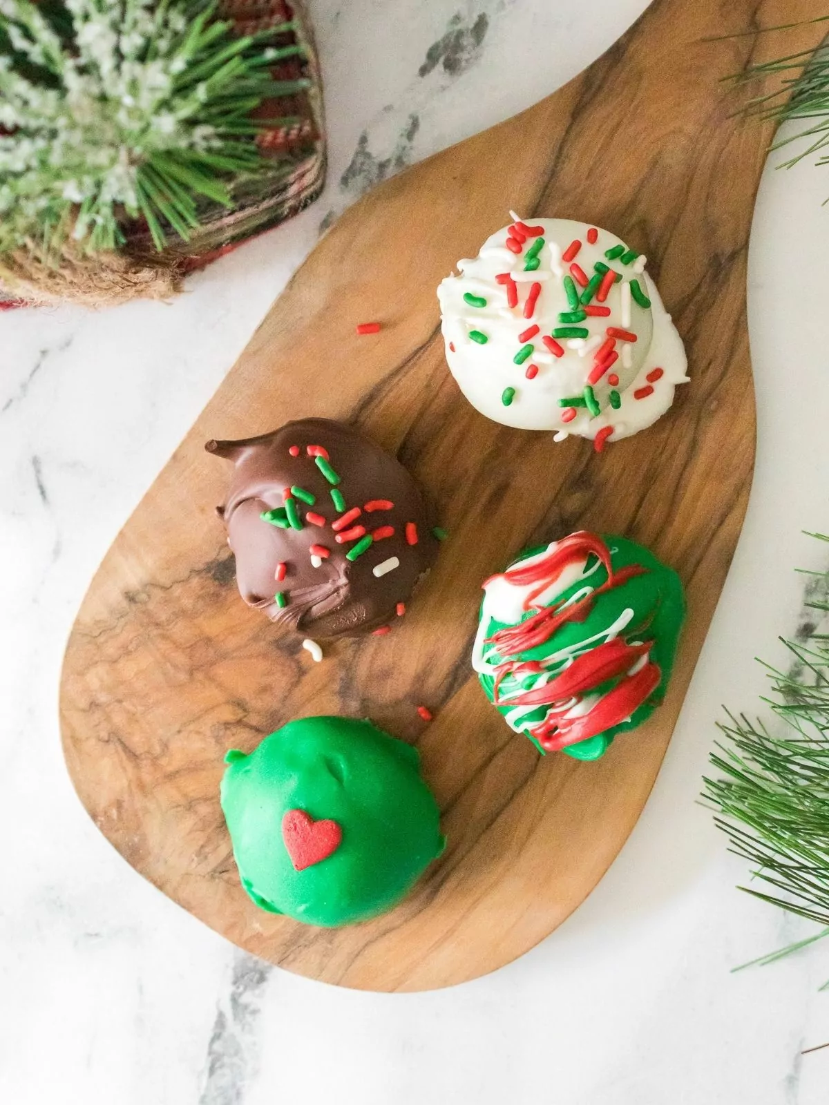 four cookie balls dipped in different colored chocolate on cutting board.