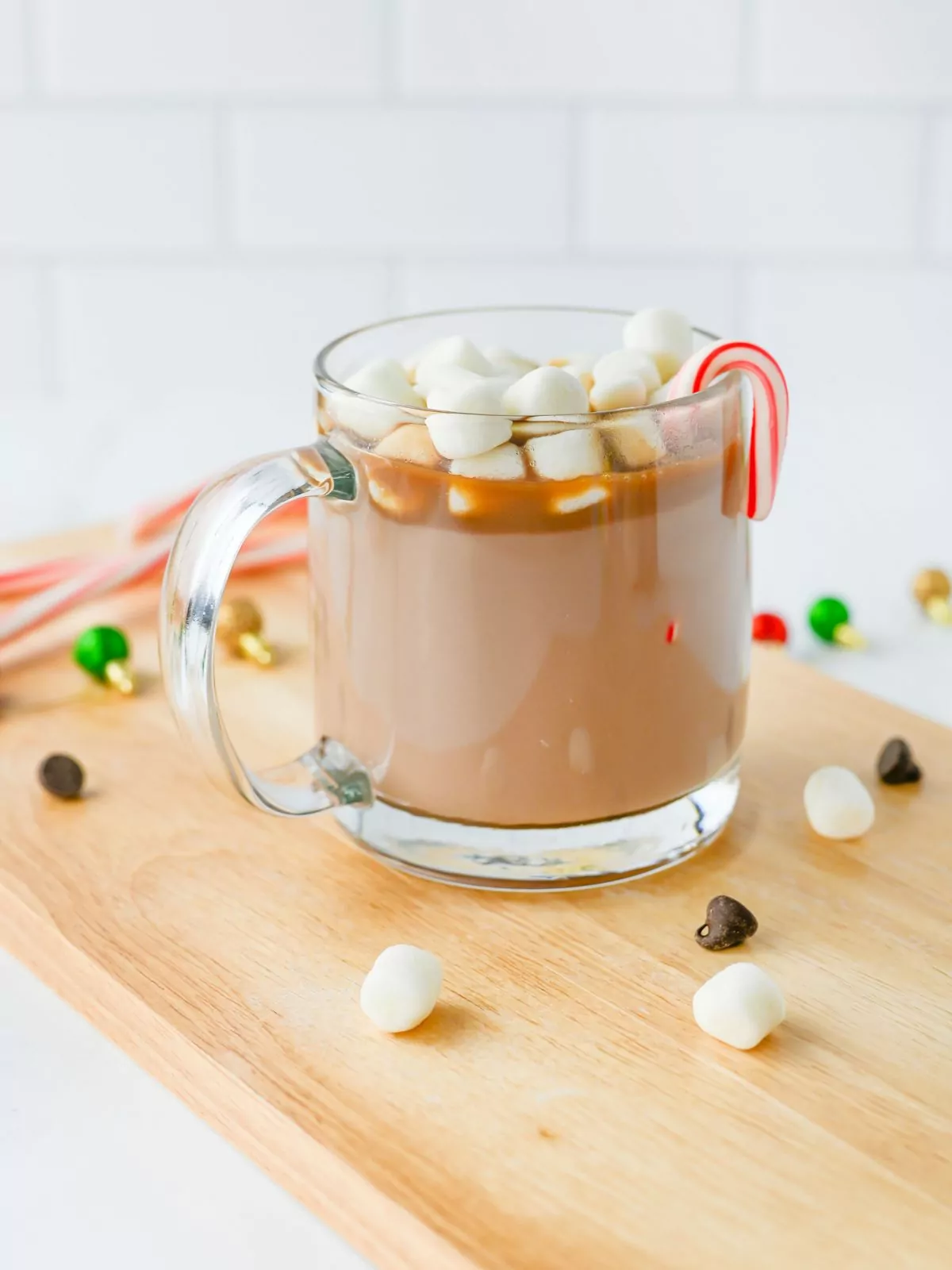 closeup of hot chocolate in a glass mug with marshmallows and peppermint candy canes.