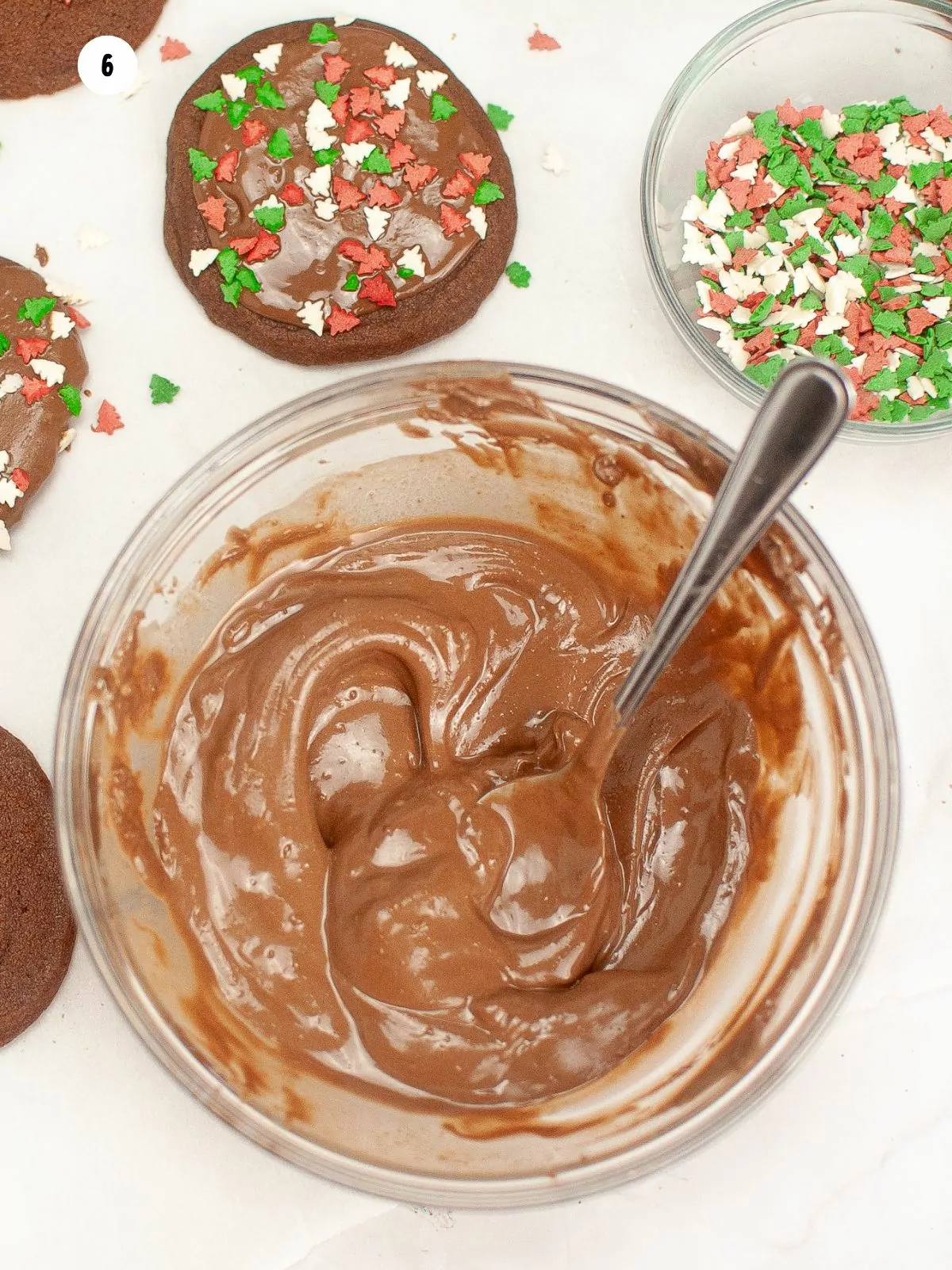 melted chocolate in bowl with chocolate cookies and sprinkles on the side.