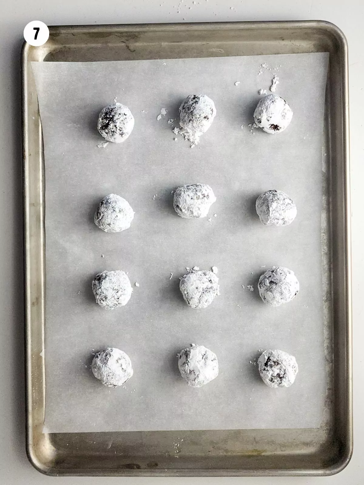 chocolate cookie dough balls rolled in powdered sugar on baking tray before baking.