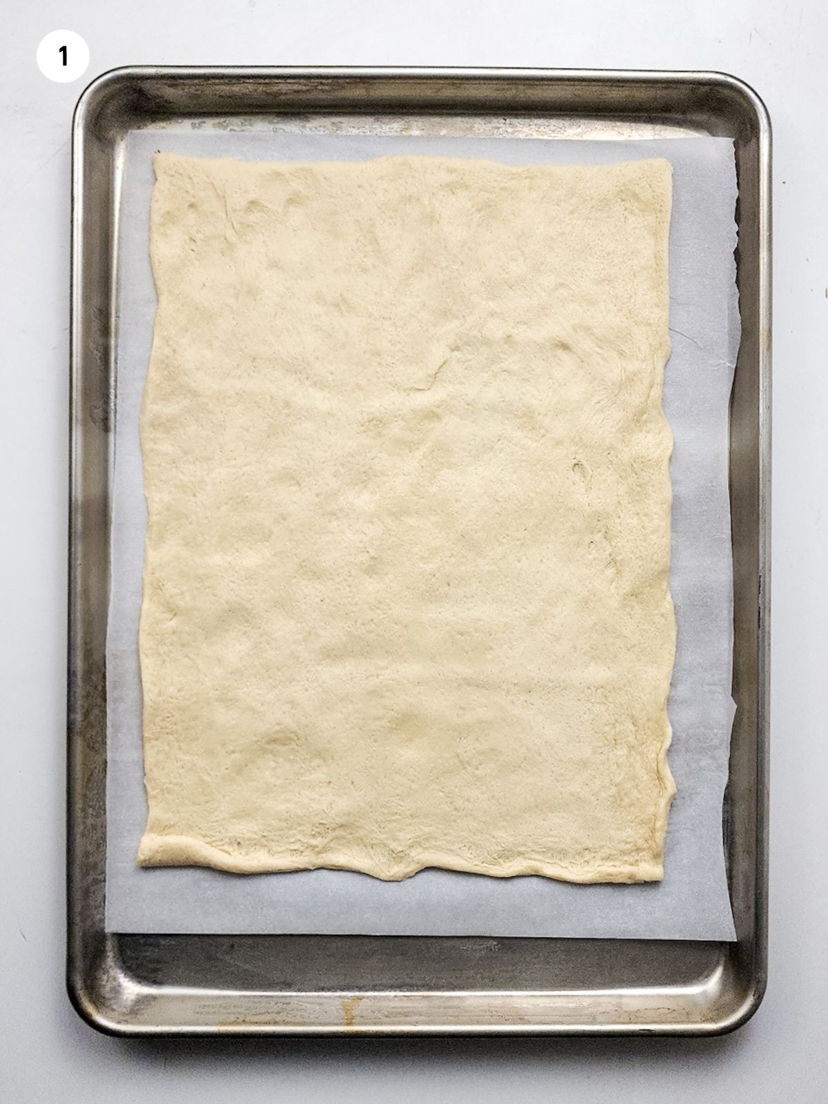 crescent roll sheet dough spread out on baking tray and parchment paper.