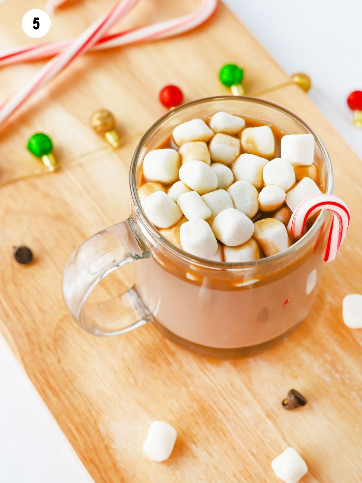 close up of hot chocolate in a mug with marshmallows on cutting board.