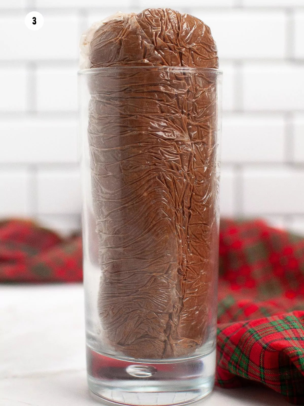 chocolate cookie dough wrapped in plastic wrap in clear glass.