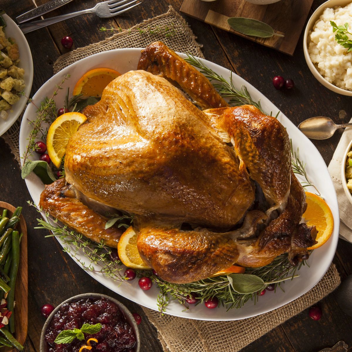 turkey roasted on platter with herbs and orange slices surrounded it.