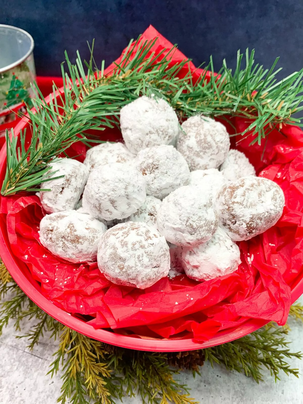 snow ball cookies in red container with pine branches.