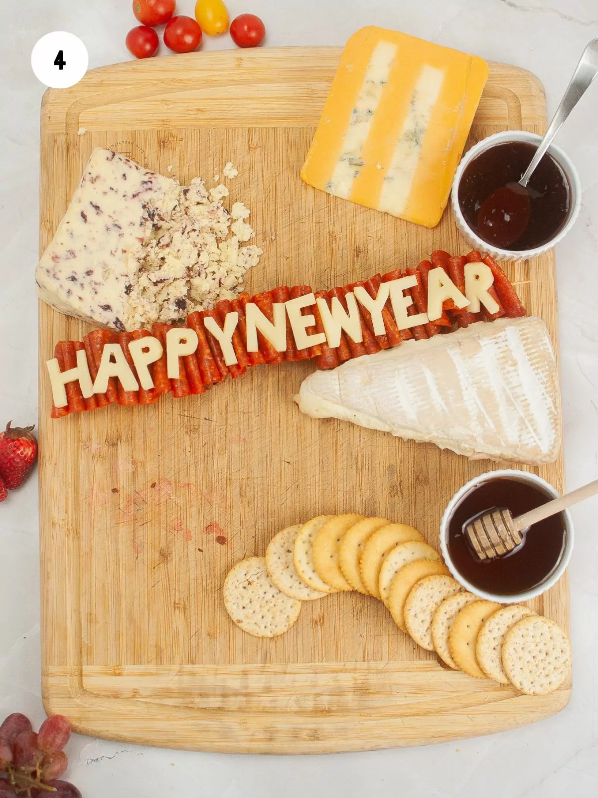 cheese letters spelling out Happy New Year on pepperoni ribbon. Small bowls of jam and honey added to board.