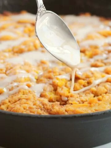 pumpkin coffee cake with powdered sugar glaze in cast iron pan.