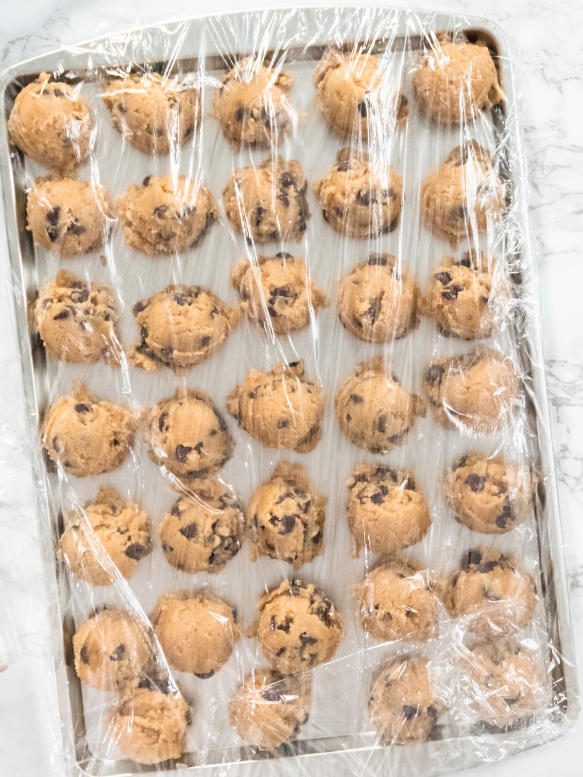 cookie dough balls wrapped in plastic wrap on baking tray.