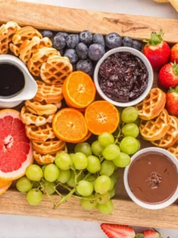 Charcuterie board with fruit, waffles, syrup, jam and chocolate spread.