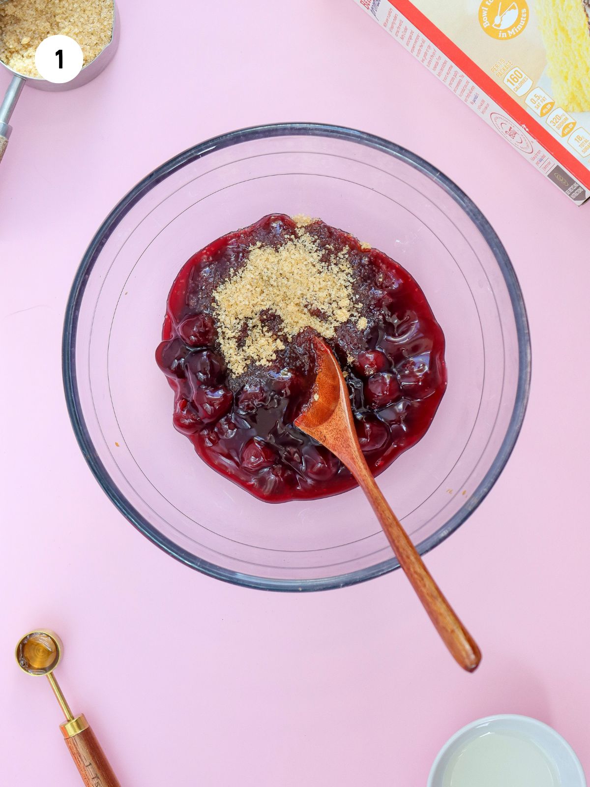 brown sugar and cherry pie filling in a clear mixing bowl with a red spoon