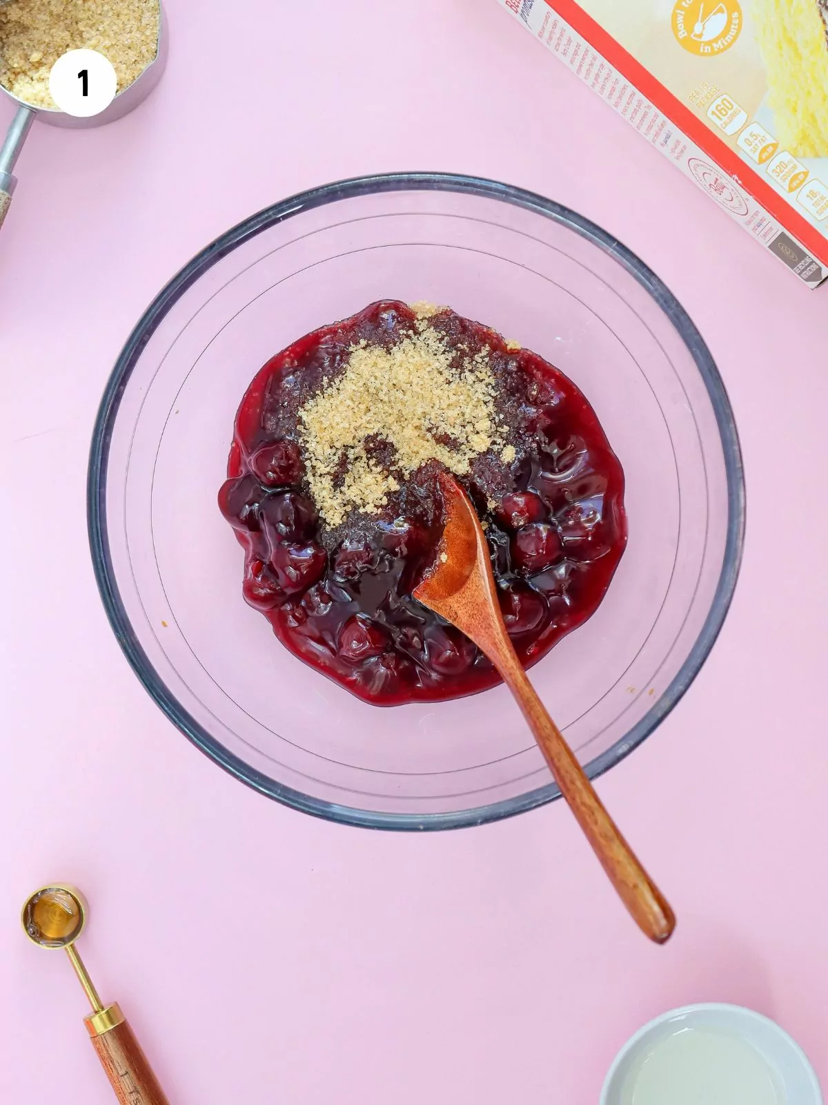 brown sugar and cherry pie filling in a clear mixing bowl with a red spoon