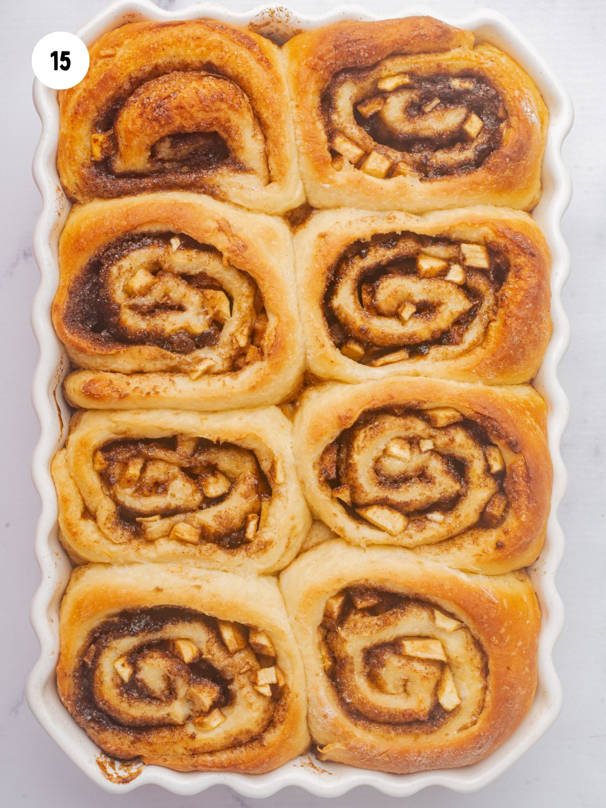 baked cinnamon rolls in a white scalloped edged baking dish