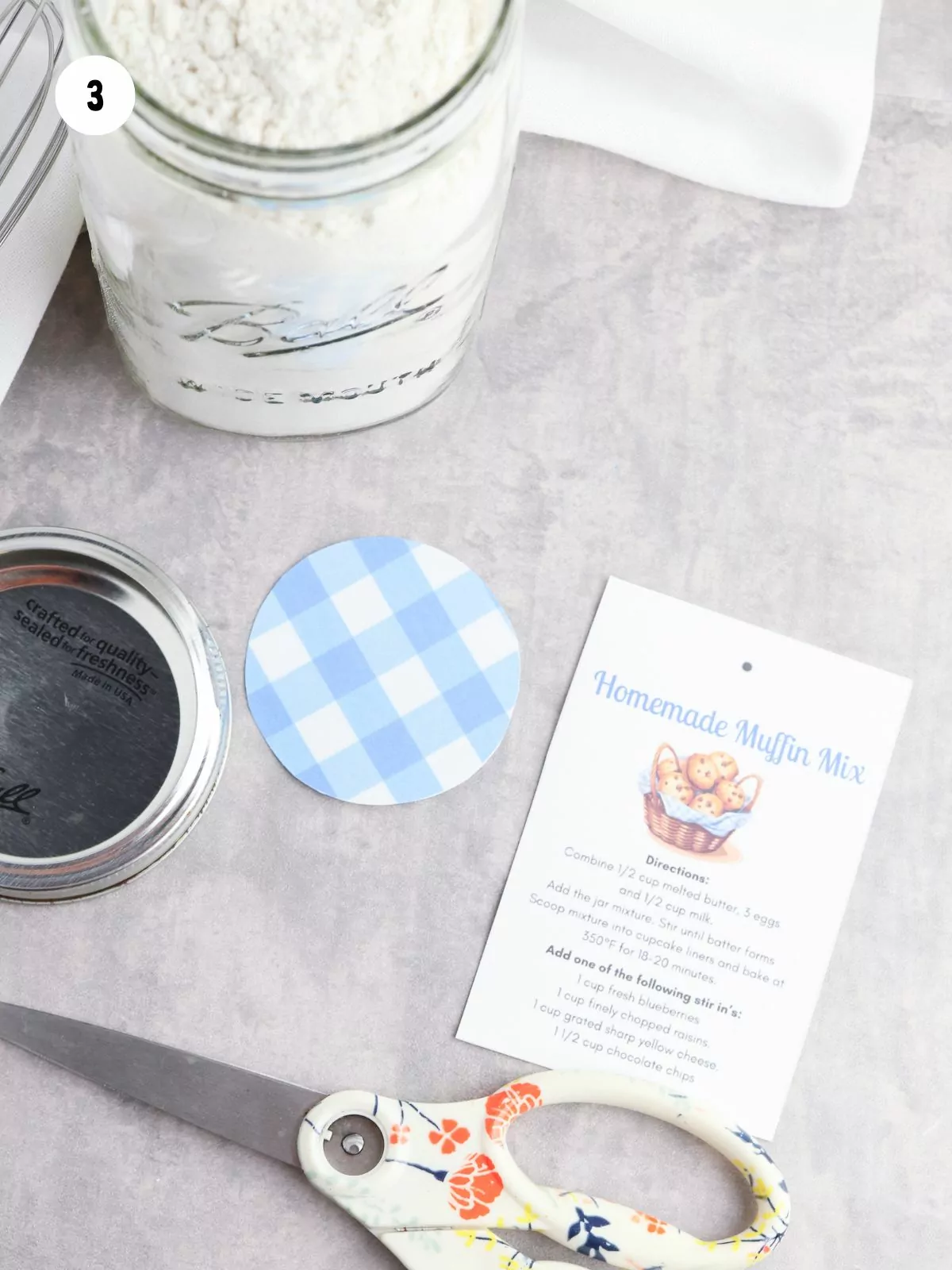 instruction card, gingham lid decoration, jar lid, filled jar, and a pair of scissors