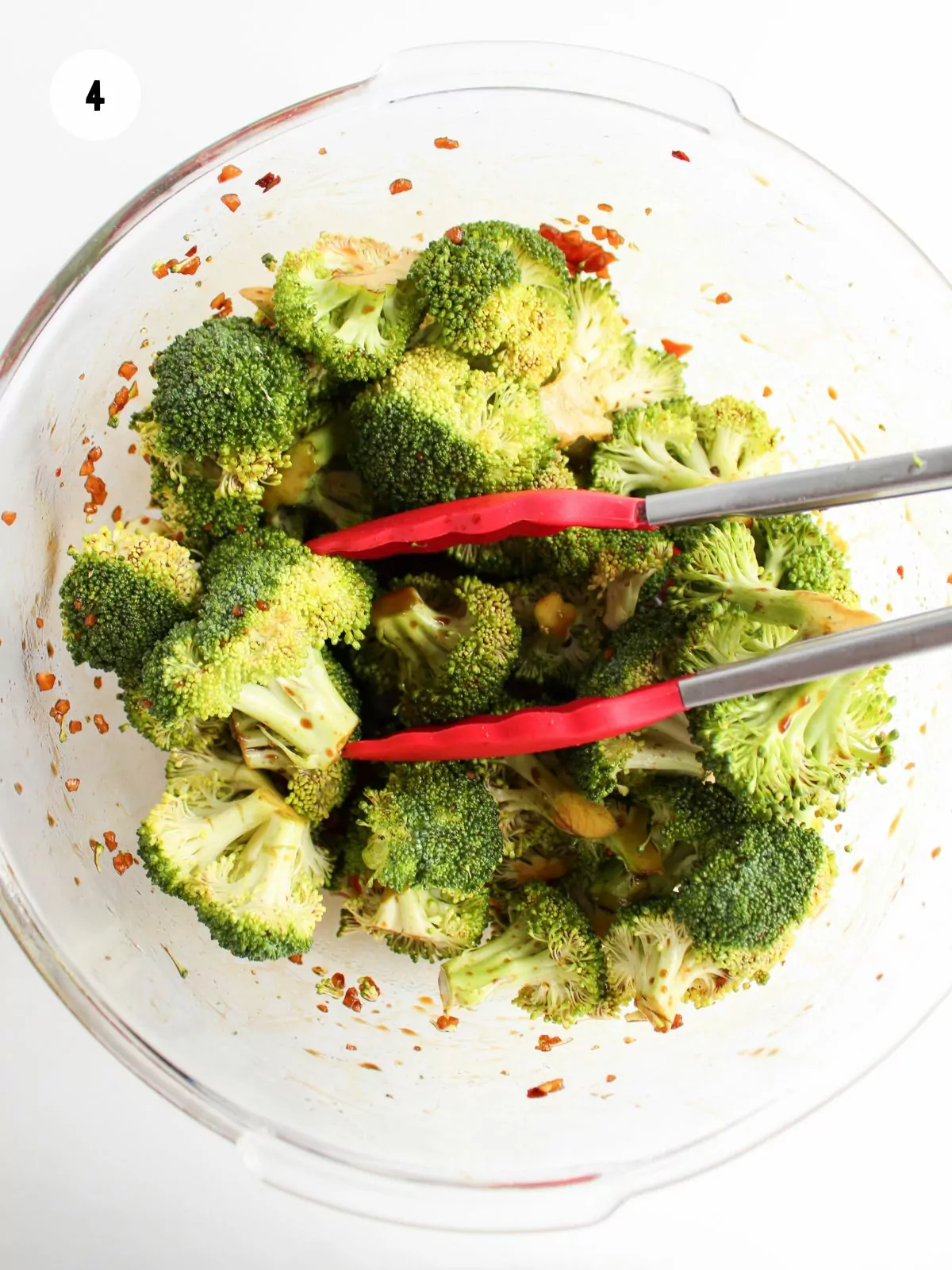 broccoli florets and tongs in a clear mixing bowl with remaining marinade