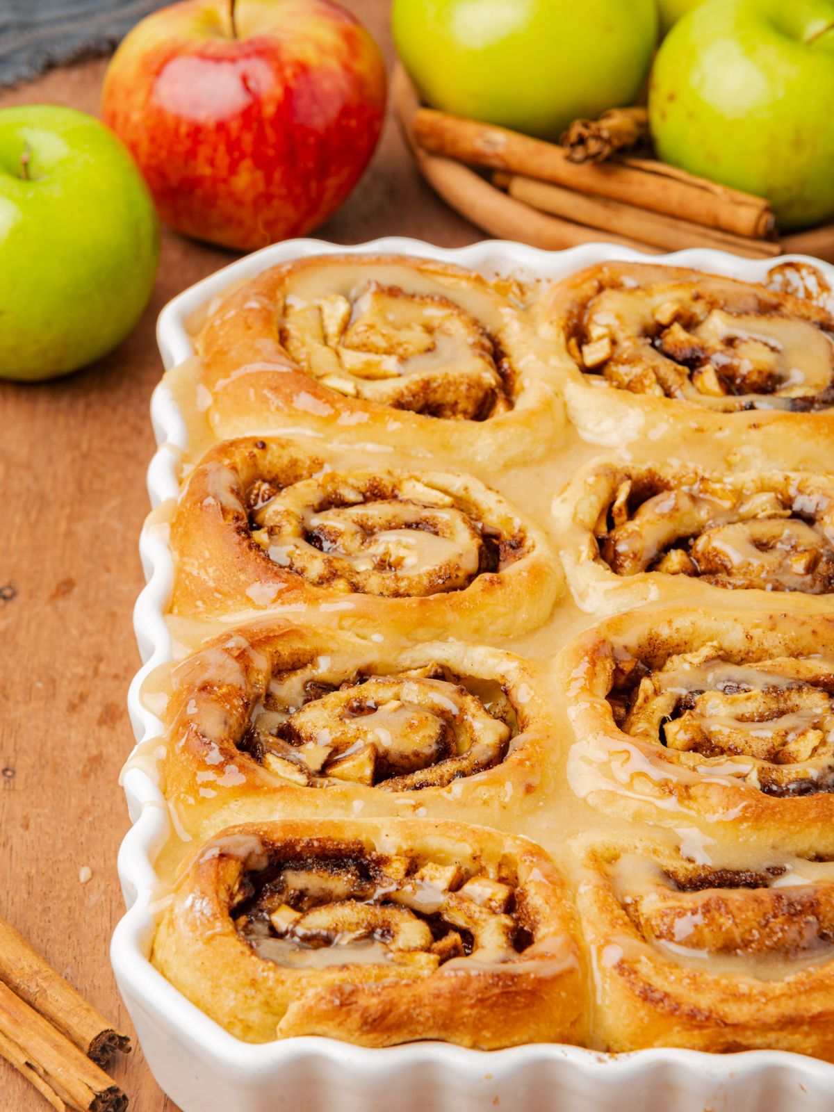 Apple Filled Cinnamon Rolls with green and red apples and cinnamon sticks in the background