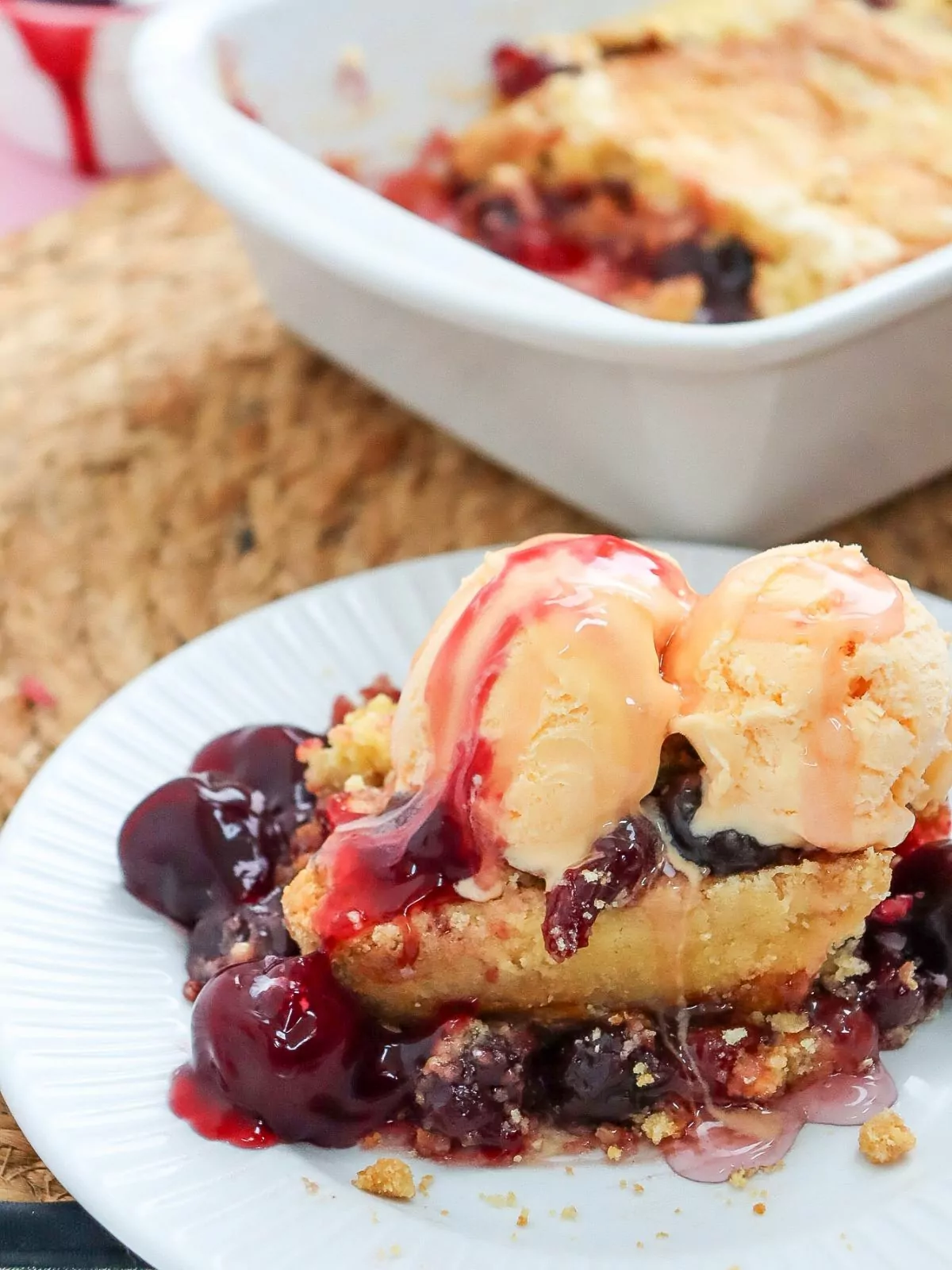 Cherry Dump Cake served on a white plate with scoops of ice cream. The dish baked in is in the background.