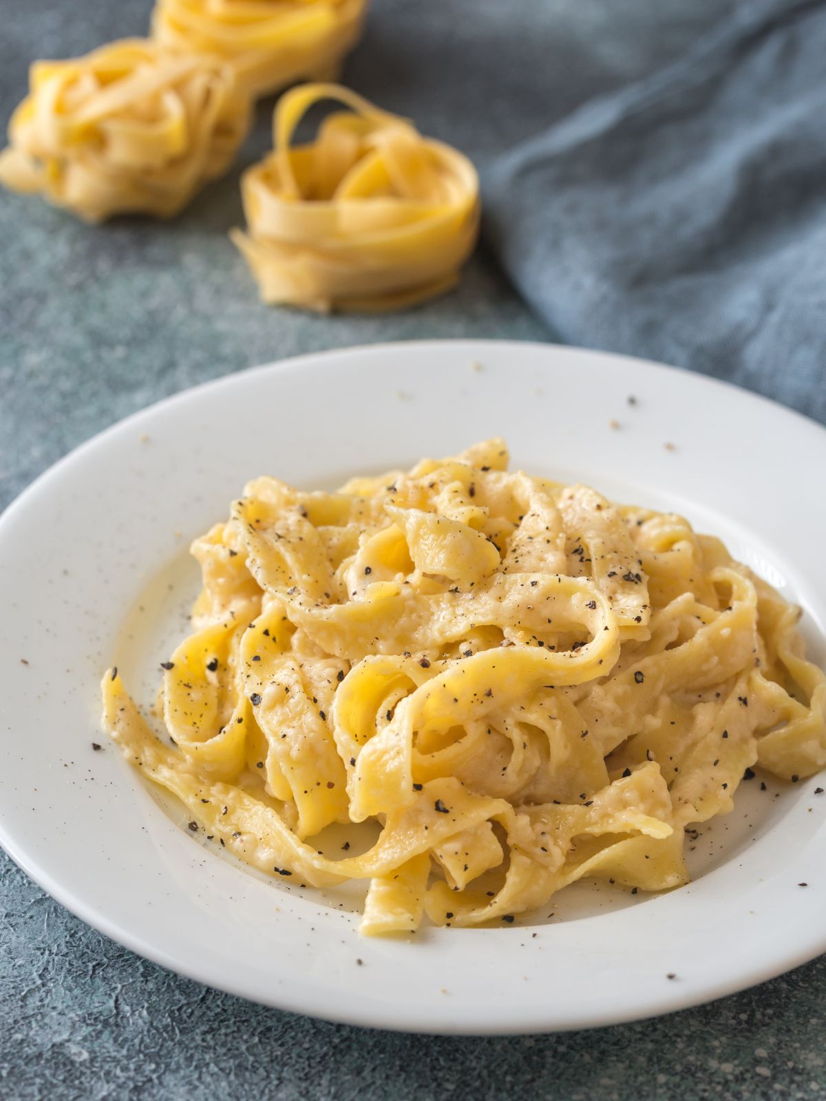 a shallow bowl of fresh fettuccine with cheese and pepper. Piles of fresh pasta in the background