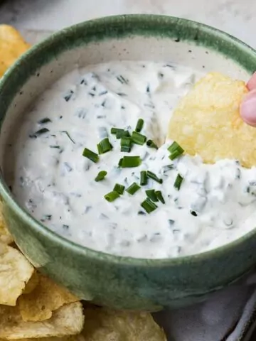 creamy dip with chives in green bowl with chips.