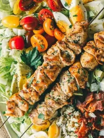 grilled chicken on skewers on top of salad greens, tomatoes, onions and bacon.