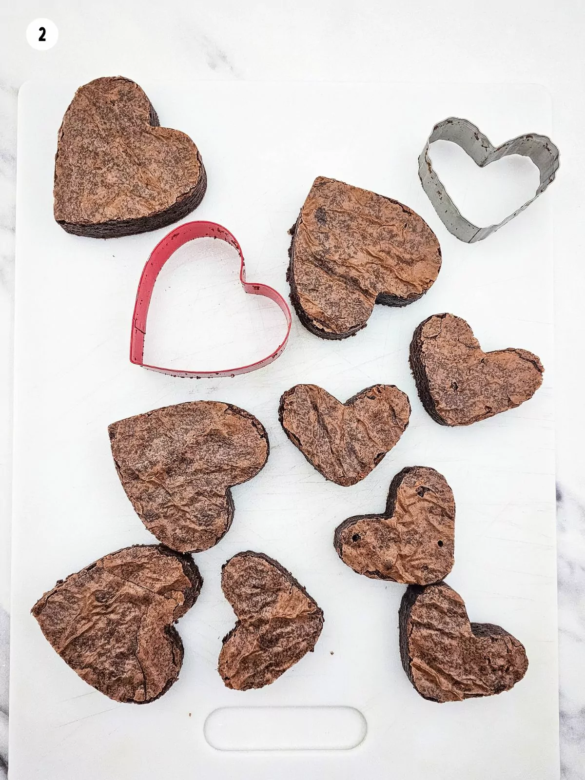 brownies cut out into hearts on white cutting board.