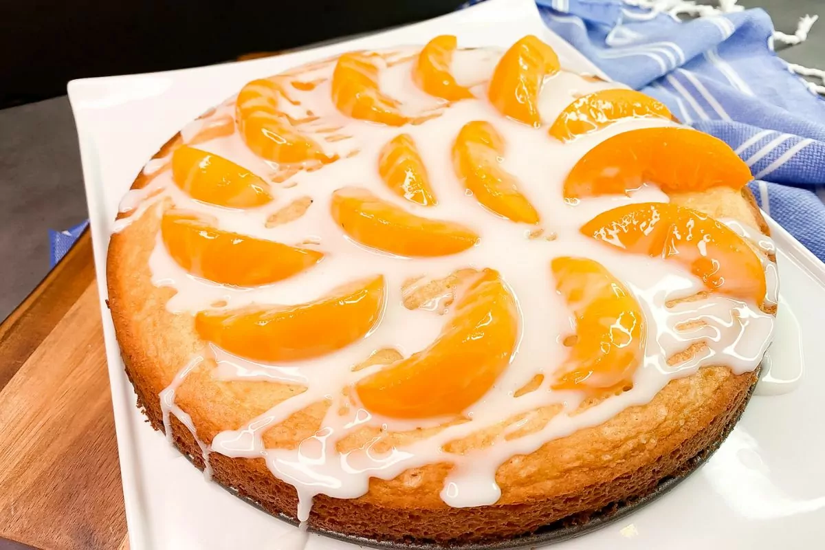 peach cake with powdered sugar glaze on serving platter.