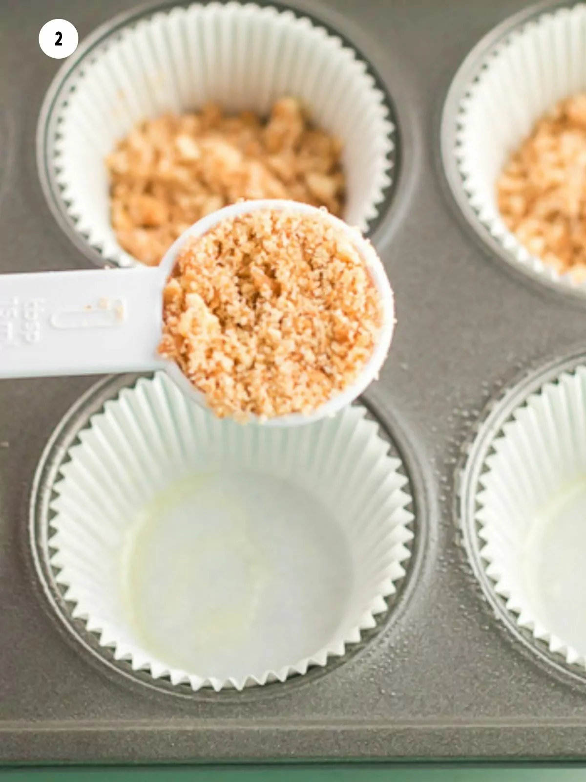 tablespoon holding cookie crumbs over muffin pan with paper liners.