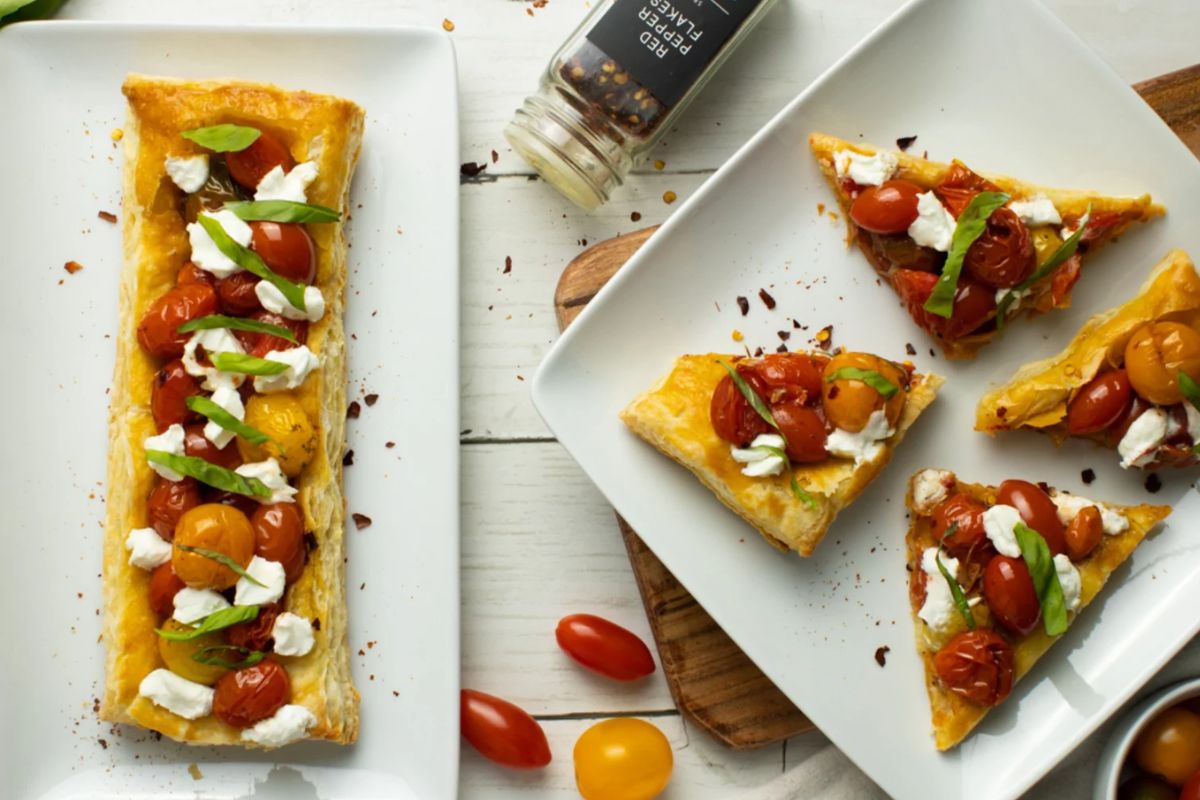 Mini tomato tarts topped with sliced tomatoes and fresh herbs.