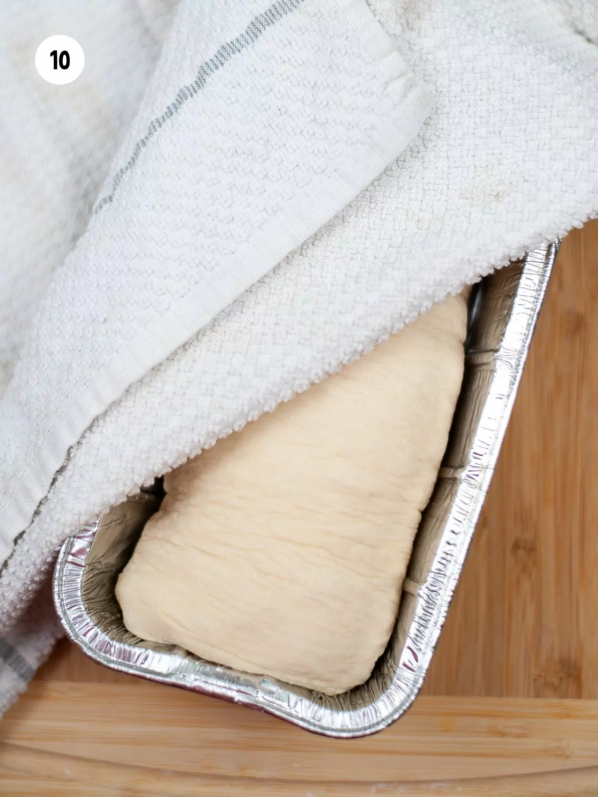 dough in a disposable loaf pan covered with towel