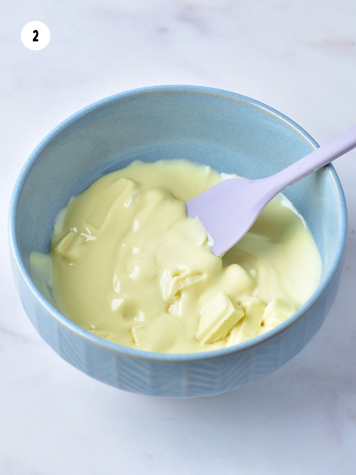 blue bowl with melted white chocolate and a lavender spatula