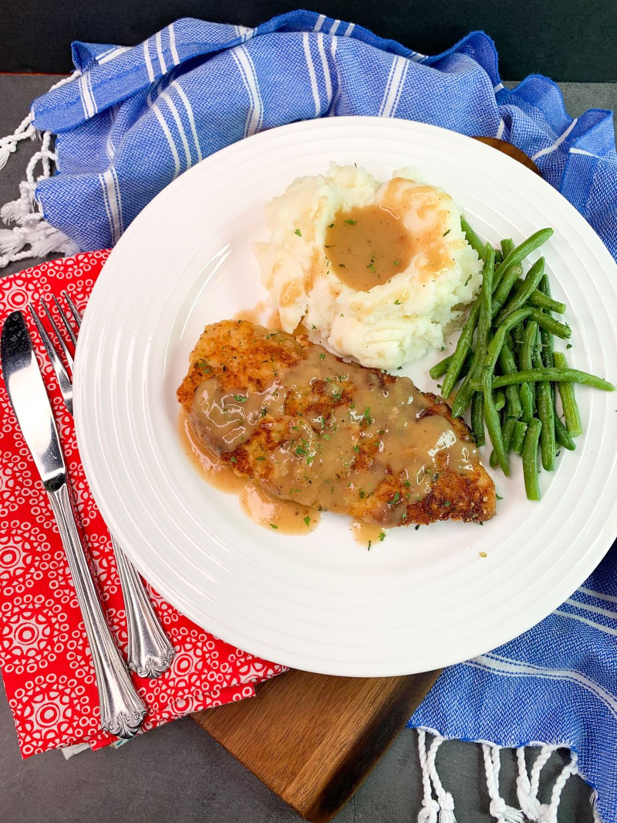 chicken cutlets with gravy, mashed potatoes and green beans on white plate.