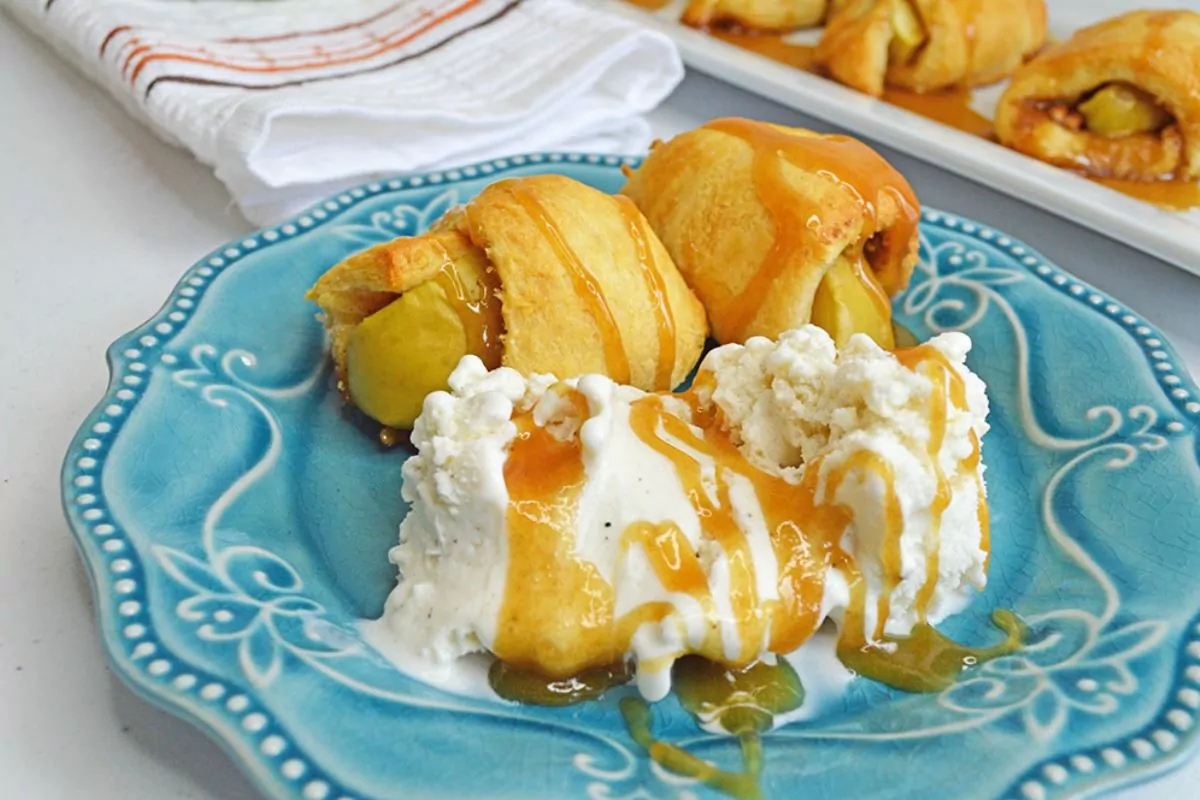 crescent rolls with apples and vanilla ice cream with caramel sauce on blue plate.