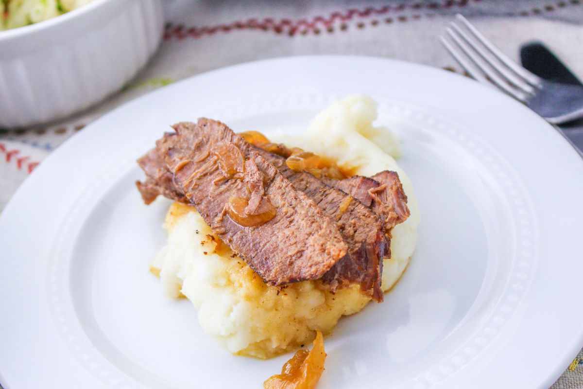 slices of flank steak and onions served over mashed potatoes on a white plate