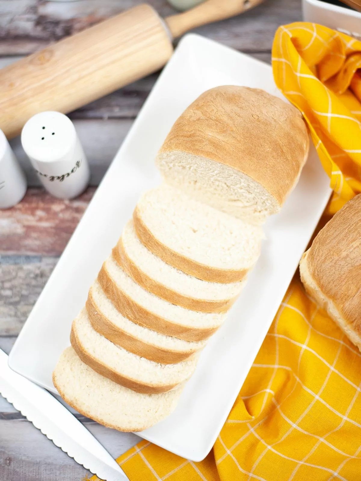 overhead view of slice Homemade White Bread on a white rectangle platter and a yellow cloth