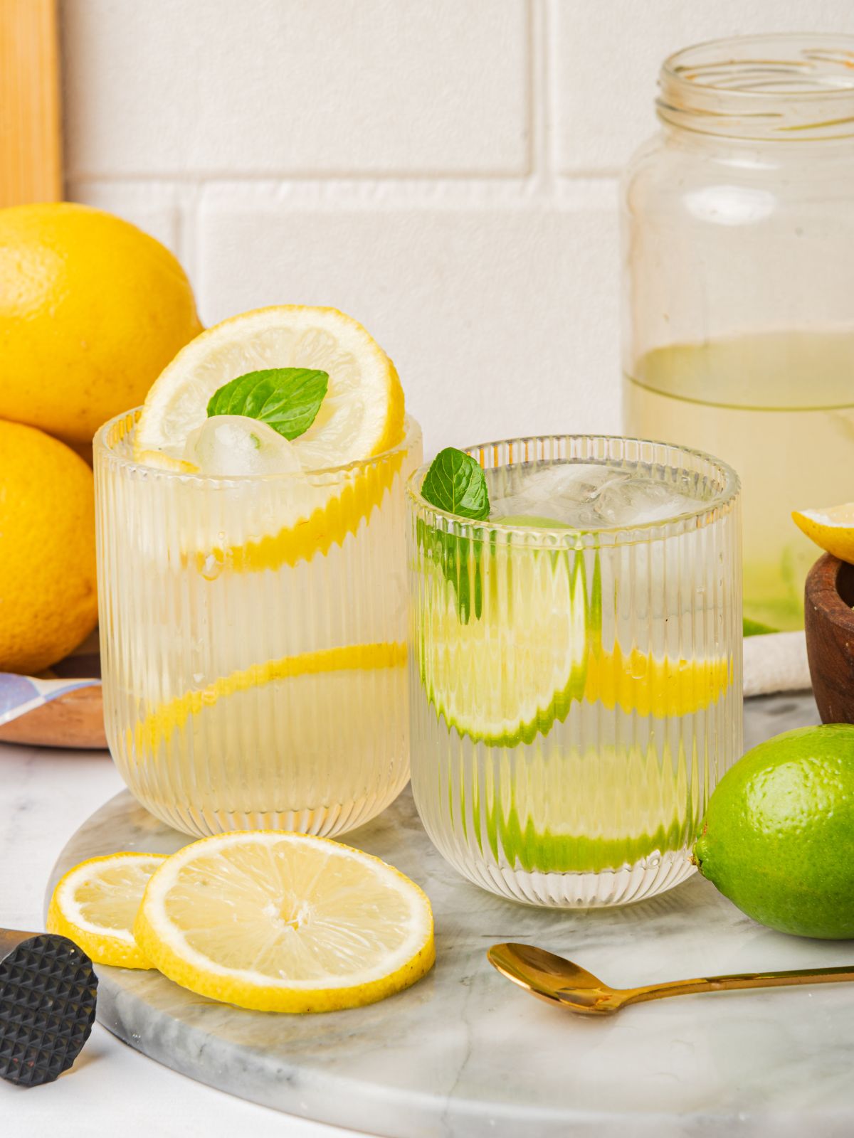 two ribbed glasses filled with water flavored with lemon and lime slices and fresh mint
