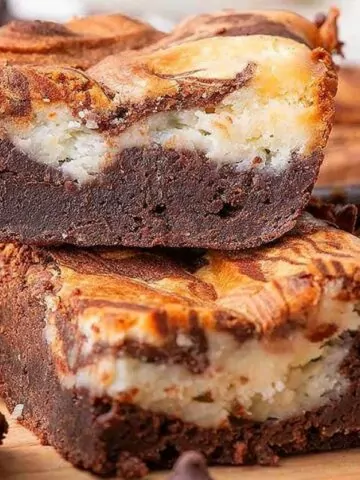 brownies with cream cheese layer stacked on cutting board.