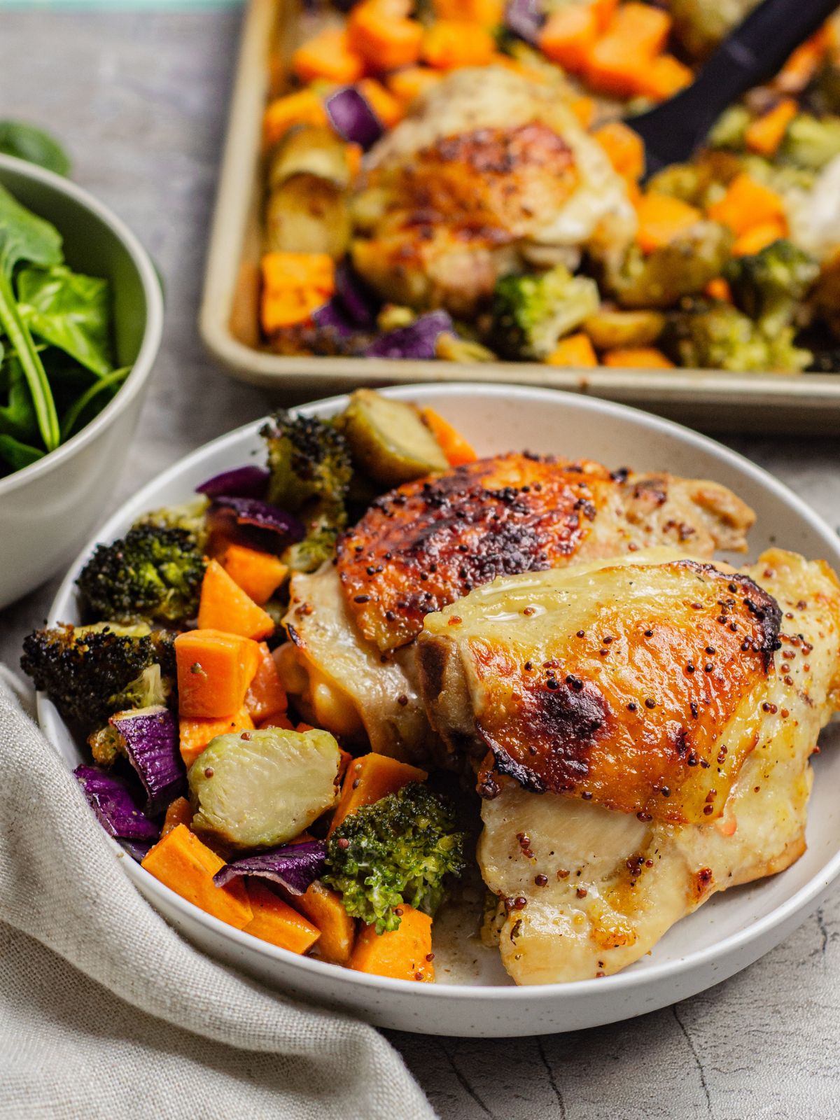 chicken thighs and veggies served on a plate with the sheet pan it was cooked on in the background