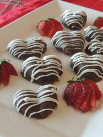 heart shaped strawberries on white platter with sliced strawberries.