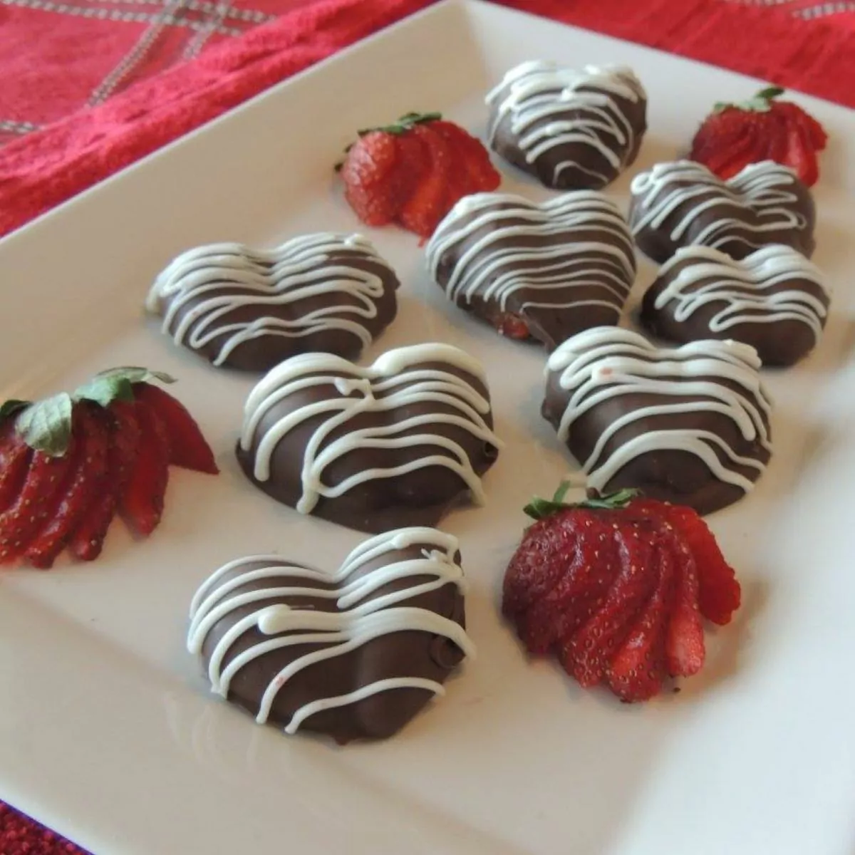 heart shaped strawberries on white platter with sliced strawberries.